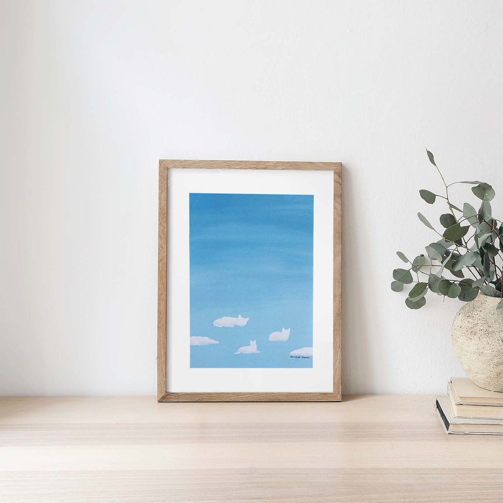Framed artwork of a blue sky with clouds on a white wall