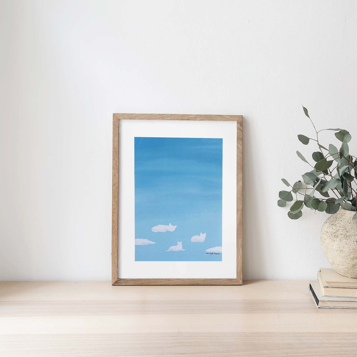 Framed artwork of a blue sky with clouds on a white wall