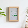 Framed print with 'Do more of what you love' text on a white wall with plants.