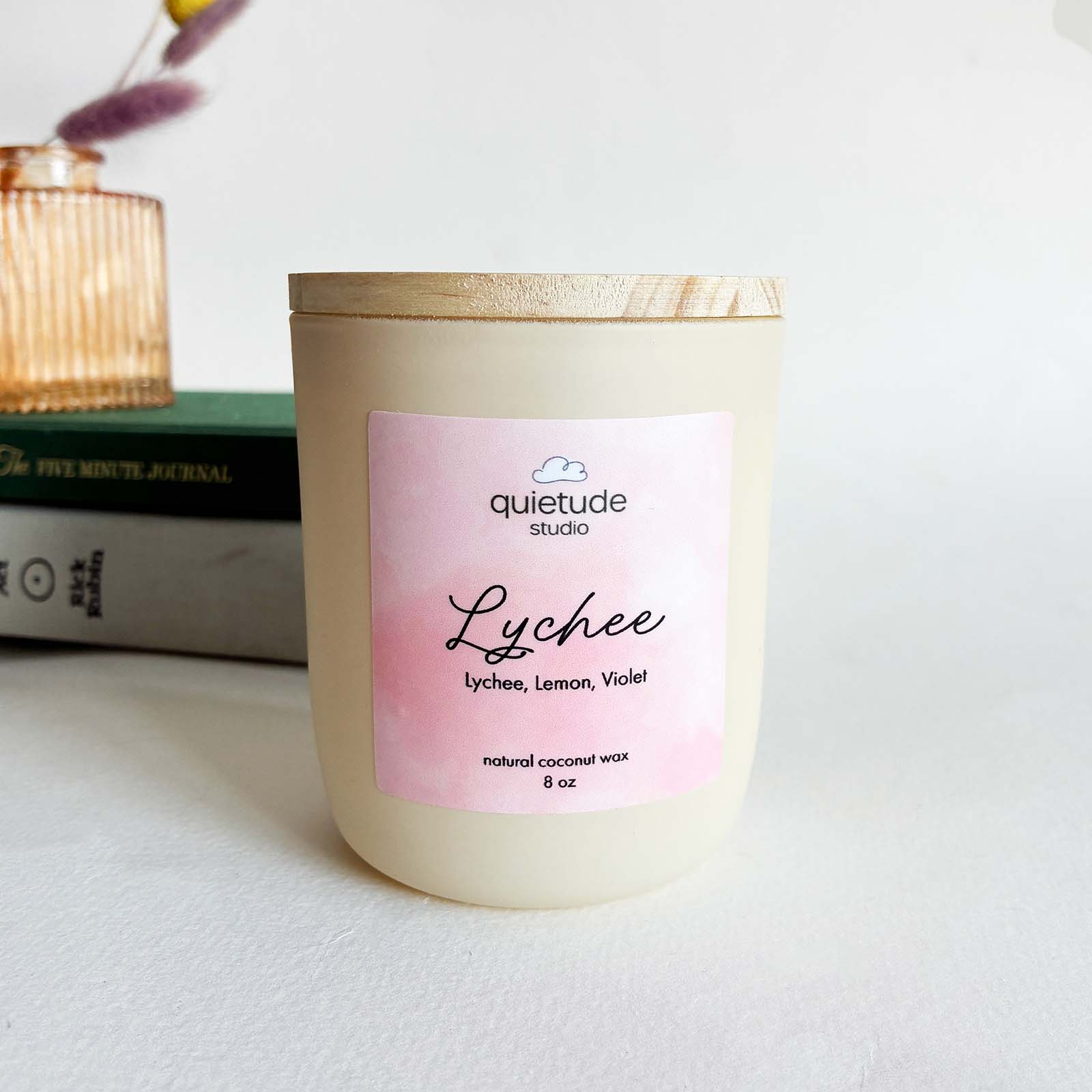 lychee soy wax candle with wooden wick in a jar on a white table with books in the background