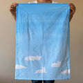 Person holding a light blue tea towel with white cat cloud patterns against a beige background