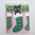 Greeting Card with a black cat in a green stocking alongside two green stockings against a light green background