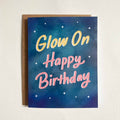 greeting card, Glow On Happy Birthday text in yellow and pink on a blue starry background, with a kraft brown envelope.