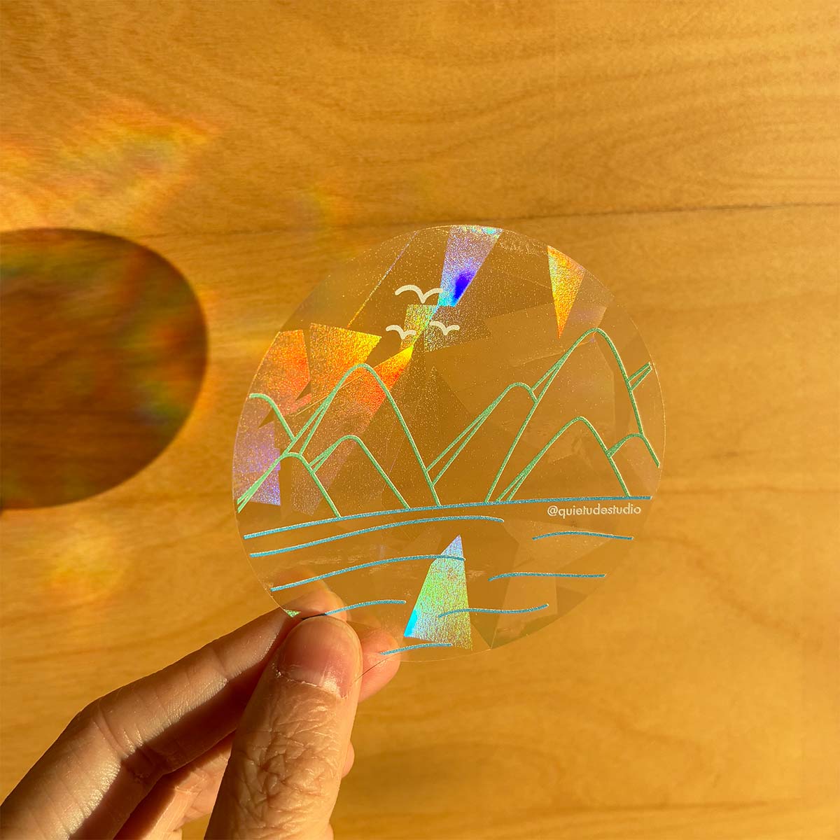 Holographic mountain design sticker held by a hand on a wooden surface