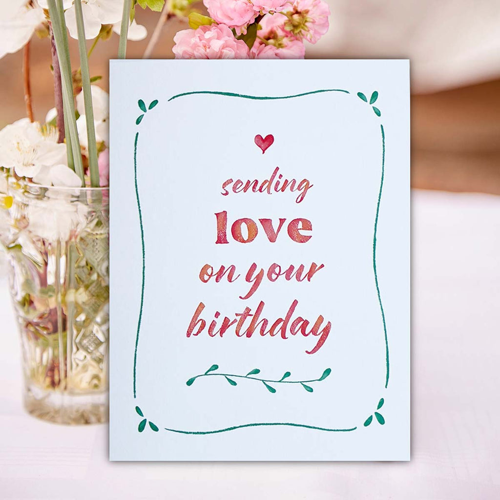 Greeting card with 'sending love on your birthday' text next to a vase of flowers, birthday card