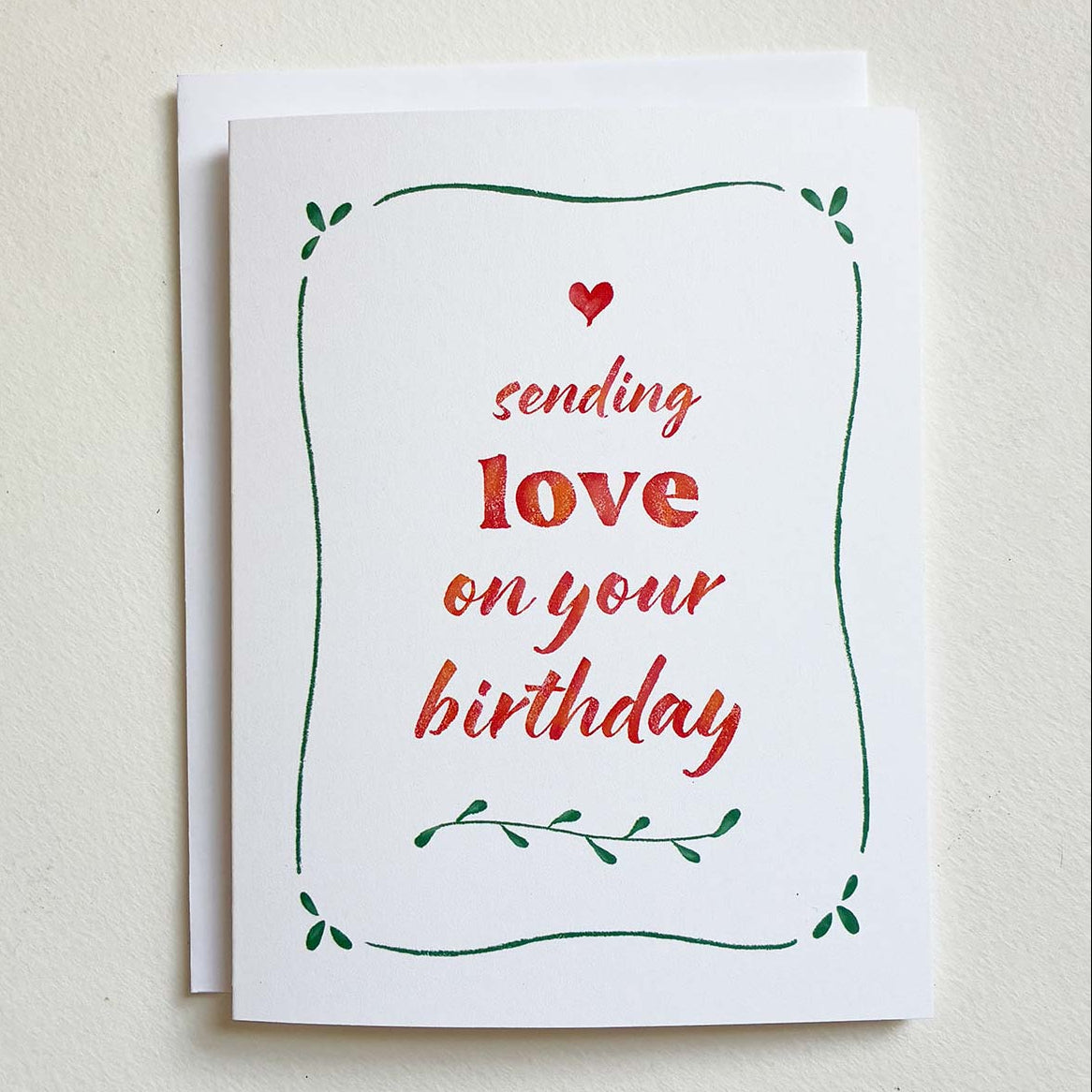 Greeting card with red text 'sending love on your birthday' and green leaves on a beige background