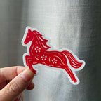 Red horse-shaped sticker held by a hand