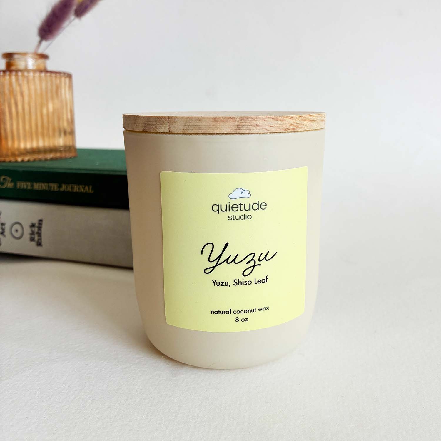 yuzu soy wax candle with wooden wick on a white table with books and small vase